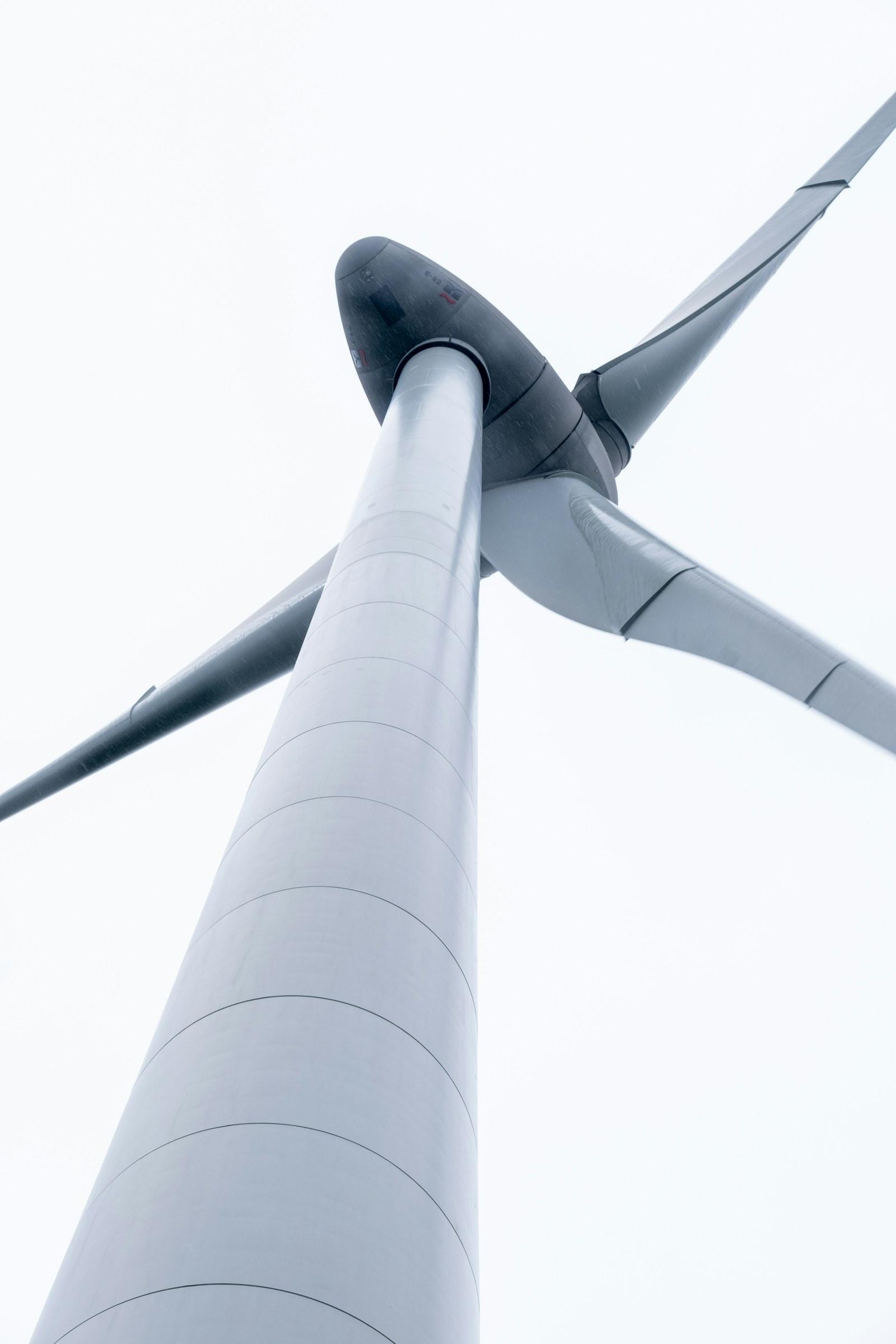 Wind turbine hub and blades seen from below against a white sky
